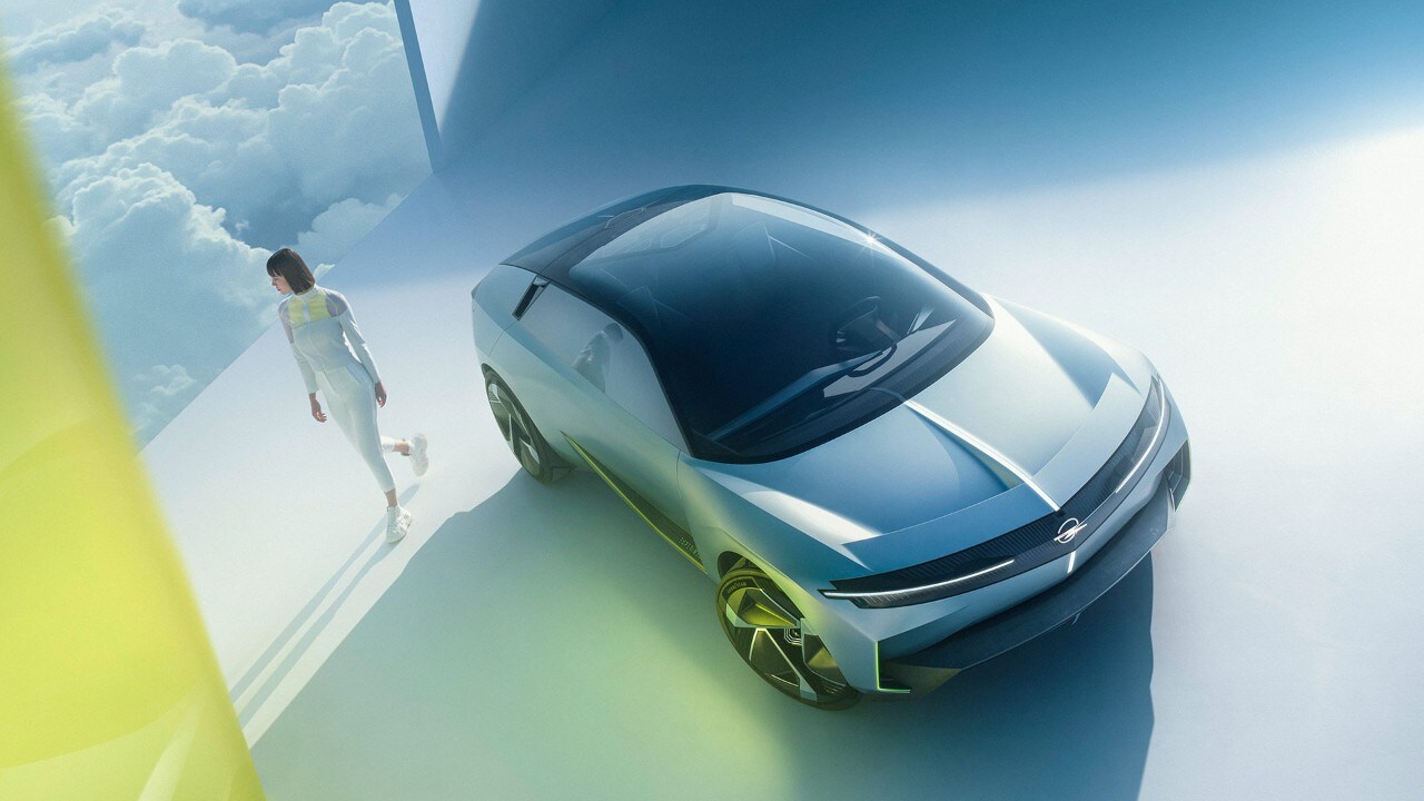 Bovenaanzicht van een zilveren Opel Experimental waar een vrouw naast loopt