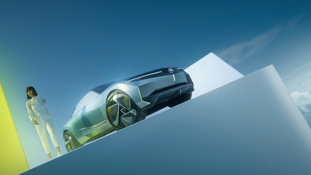 Vooraanzicht van een zilveren Opel Experimental waar een vrouw naast staat.
