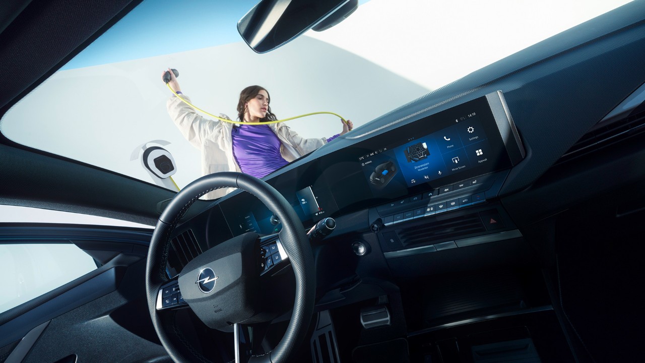 Interieur van de Opel Astra Hatchback met een vrouw die aan de buitenzijde een laadkabel vasthoudt