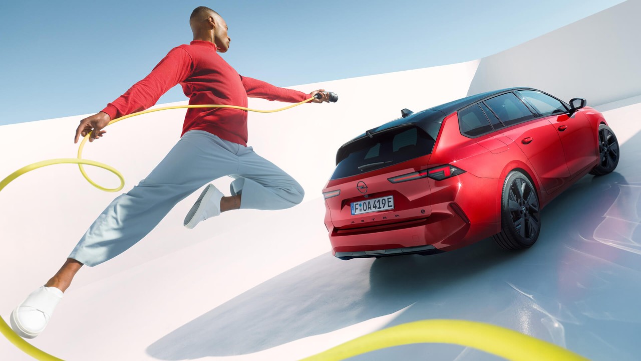 Man springt in de lucht met een EV-oplaadkabel met een Opel Astra Sports Tourer Electric op de achtergrond