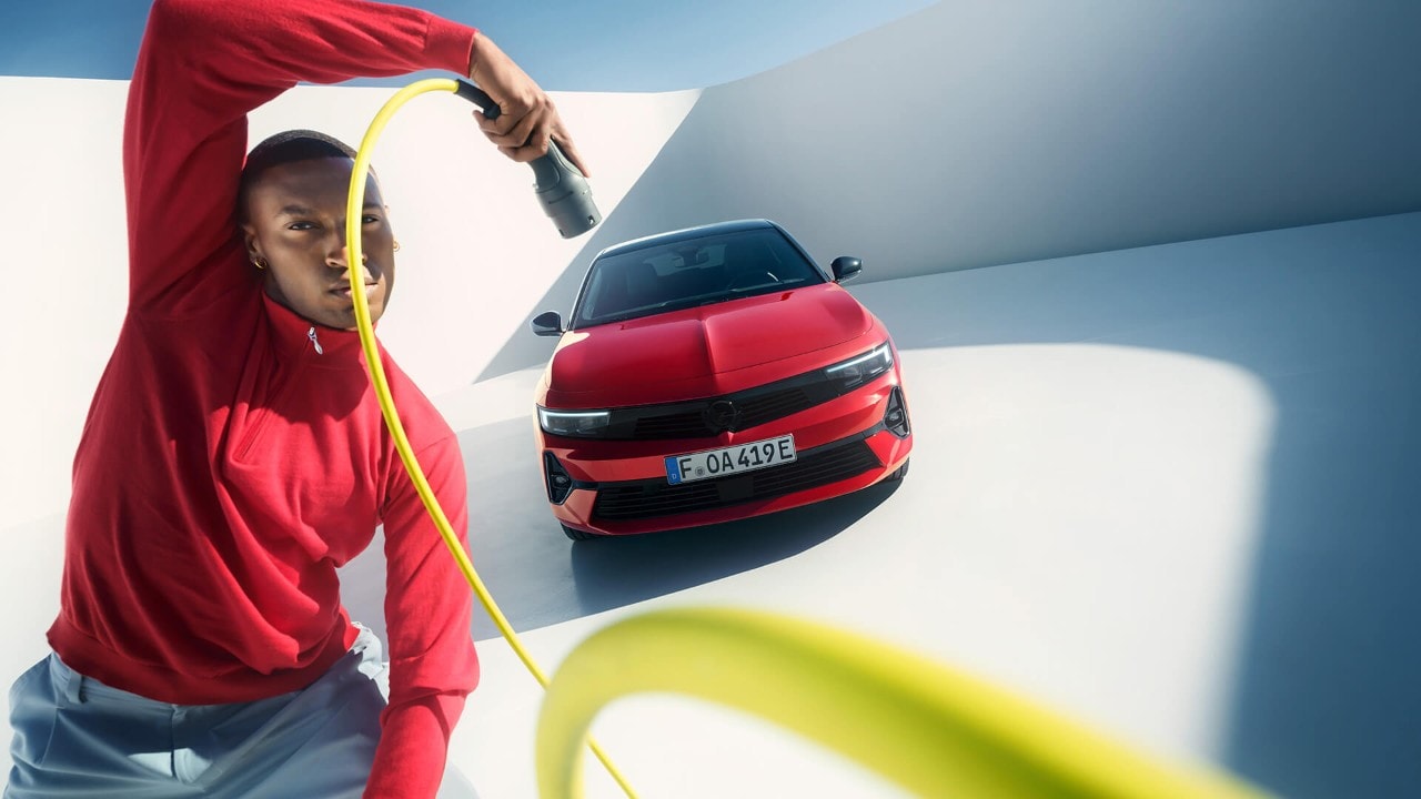 Man met EV-oplaadkabel voor een rode Opel Astra Sports Tourer met zwart dak
