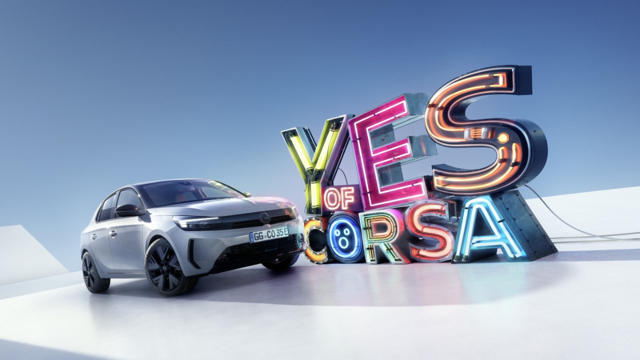 Zijaanzicht van een grijze Opel Corsa Electric met "Yes of Corsa' in de achtergrond